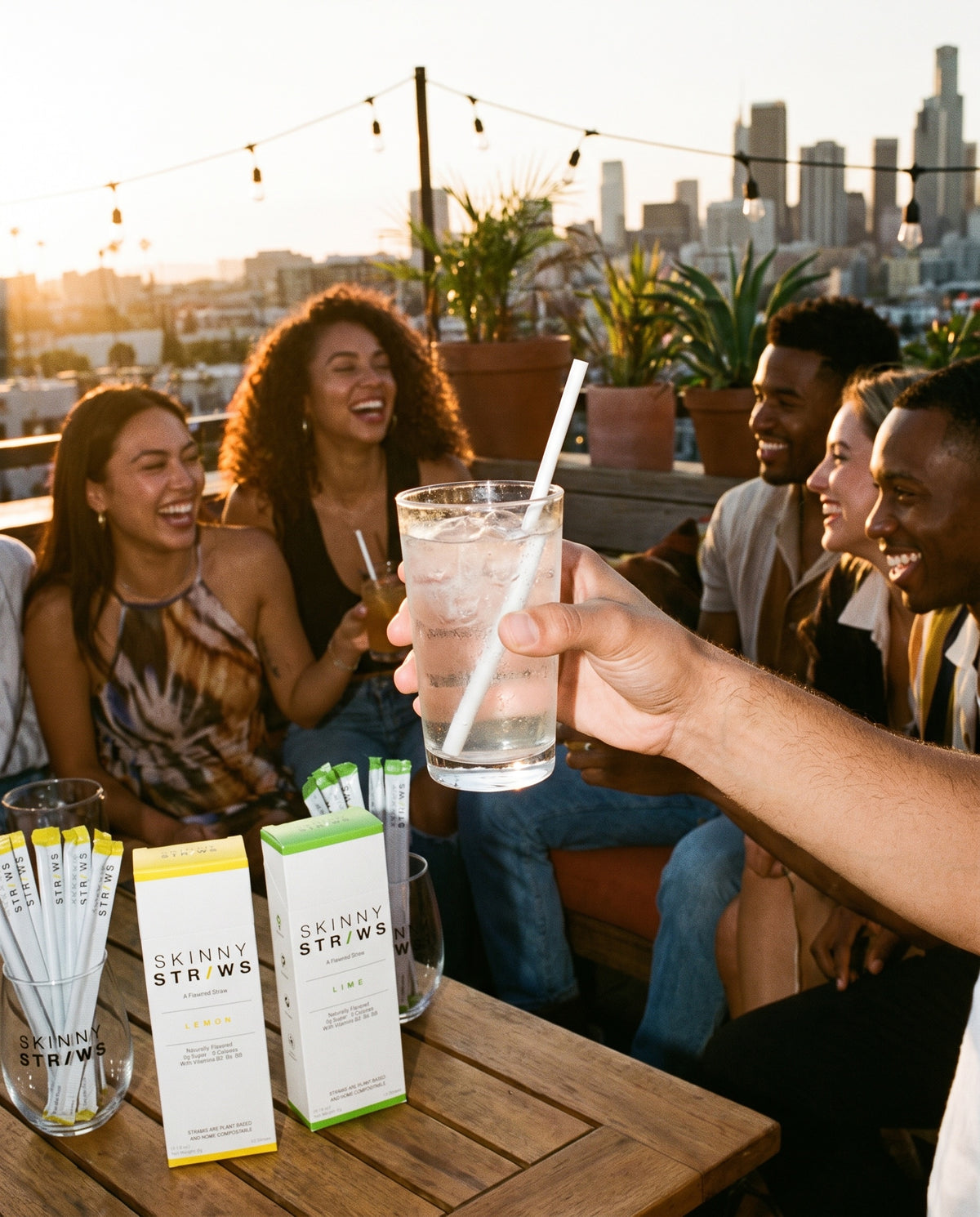 Friends on a rooftop at sunset with drinks and Skinny Straws Lemon and Lime boxes