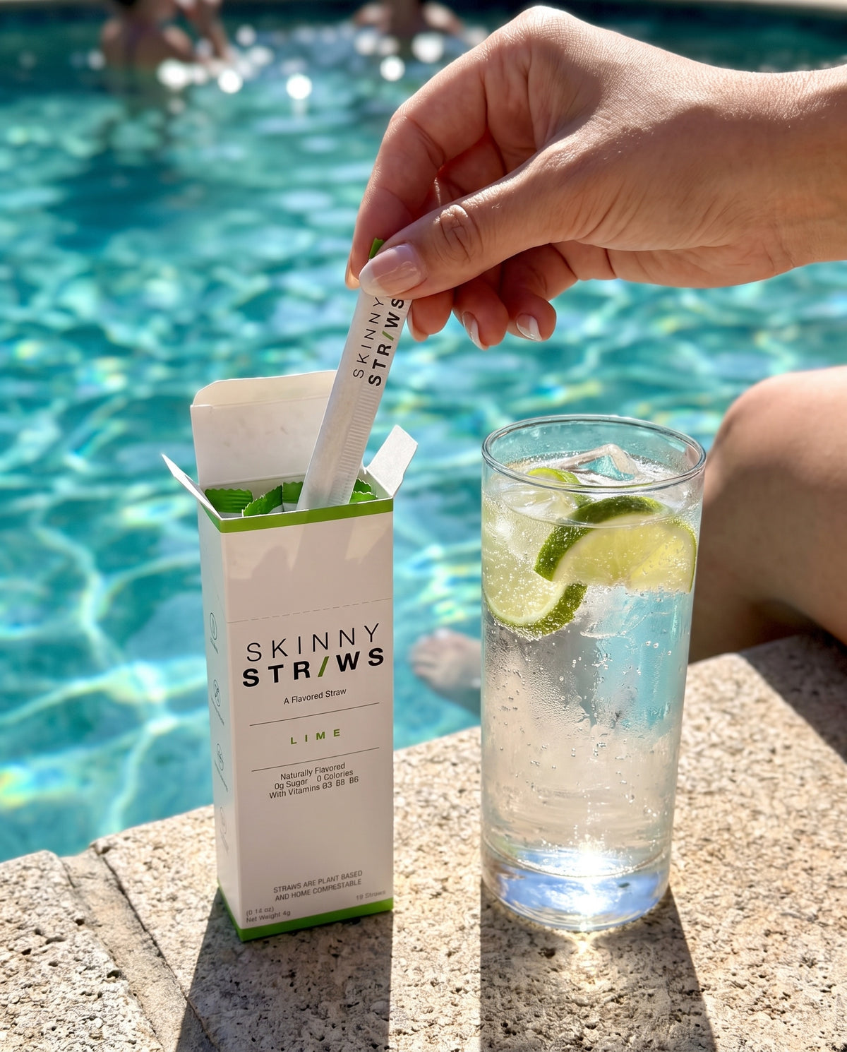 Pulling a Skinny Straws Lime straw from the box beside a sparkling drink by the pool